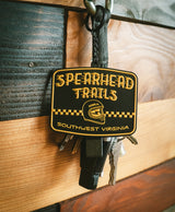 Keychain with 'Spearhead Trails' logo on a wooden surface